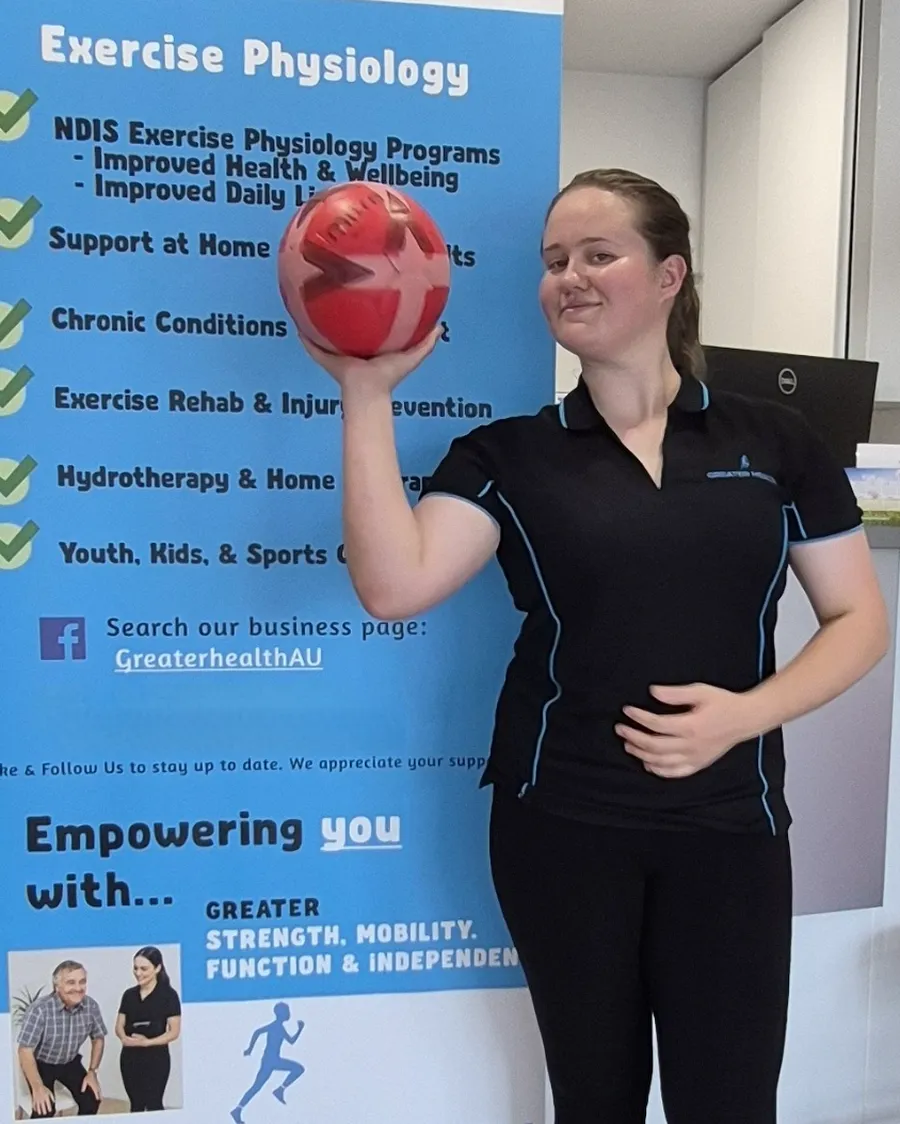 Caroline Victor, Director and Accredited Exercise Physiologist at Greater Health, holding a ball beside the Greater Health banner